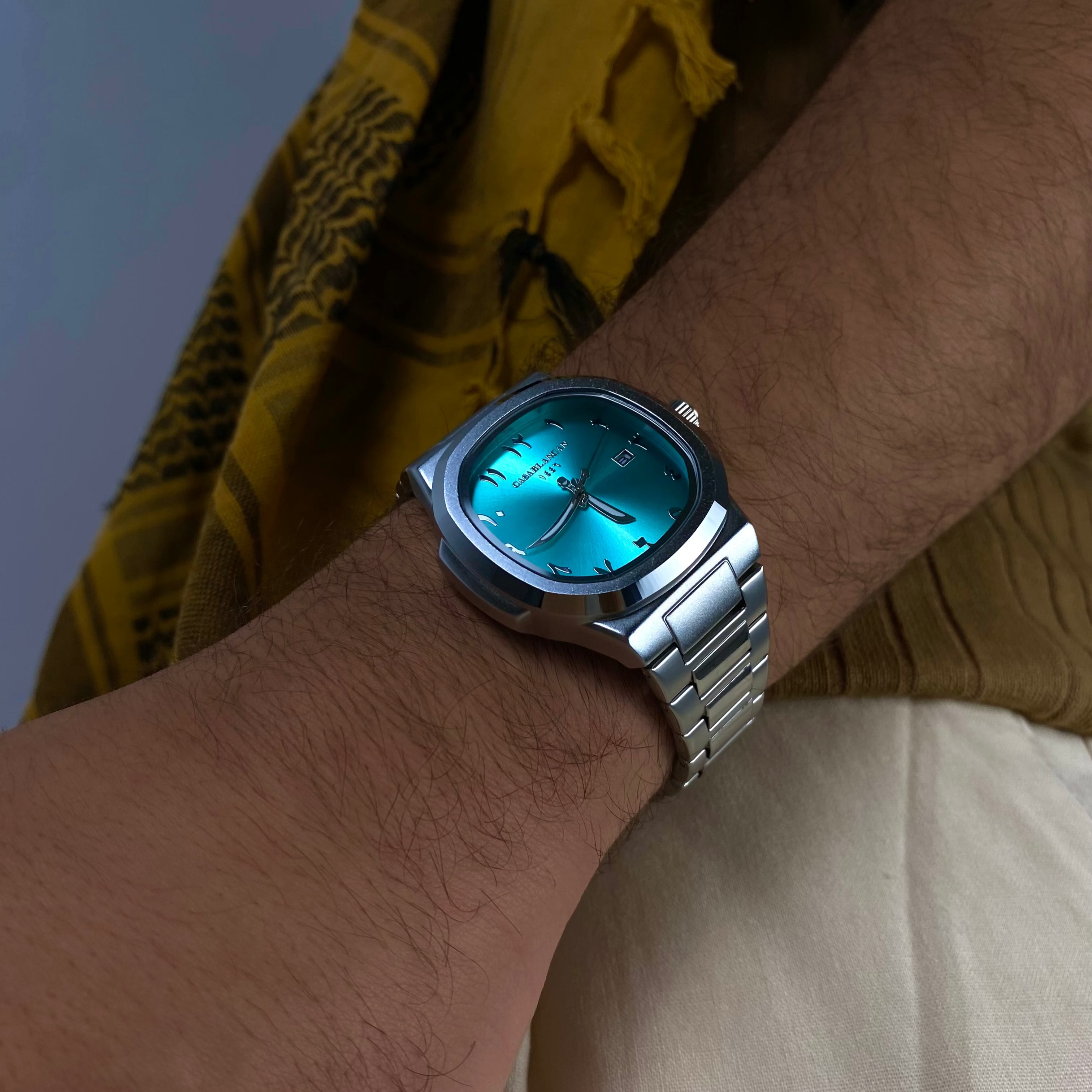 Model wearing a Casablancan Al-Majaz heritage Arabic numerals turquoise dial 43mm Watch with a yellow scarf in the background