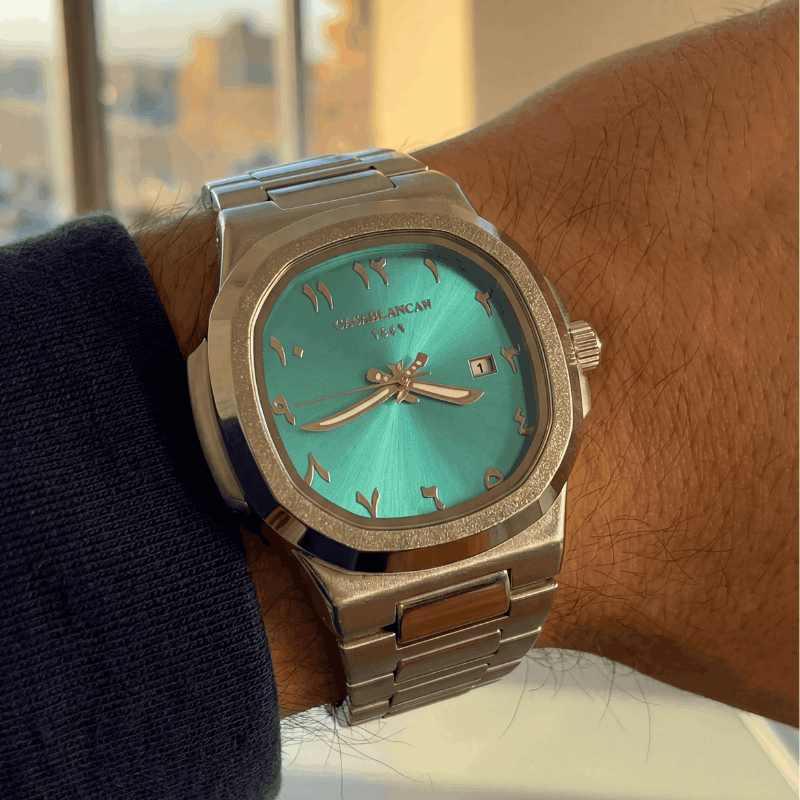 Turquoise watch with silver case on a wrist, blurred cityscape in the background