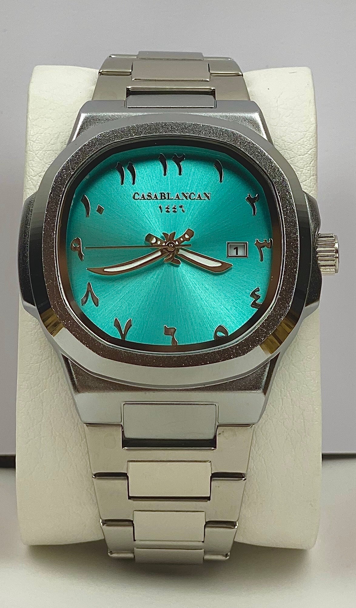 Casablancan Al-Majaz heritage Arabic numerals turquoise dial 43mm Watch with silver band and a arabic-daggers pointer signature on a white stand