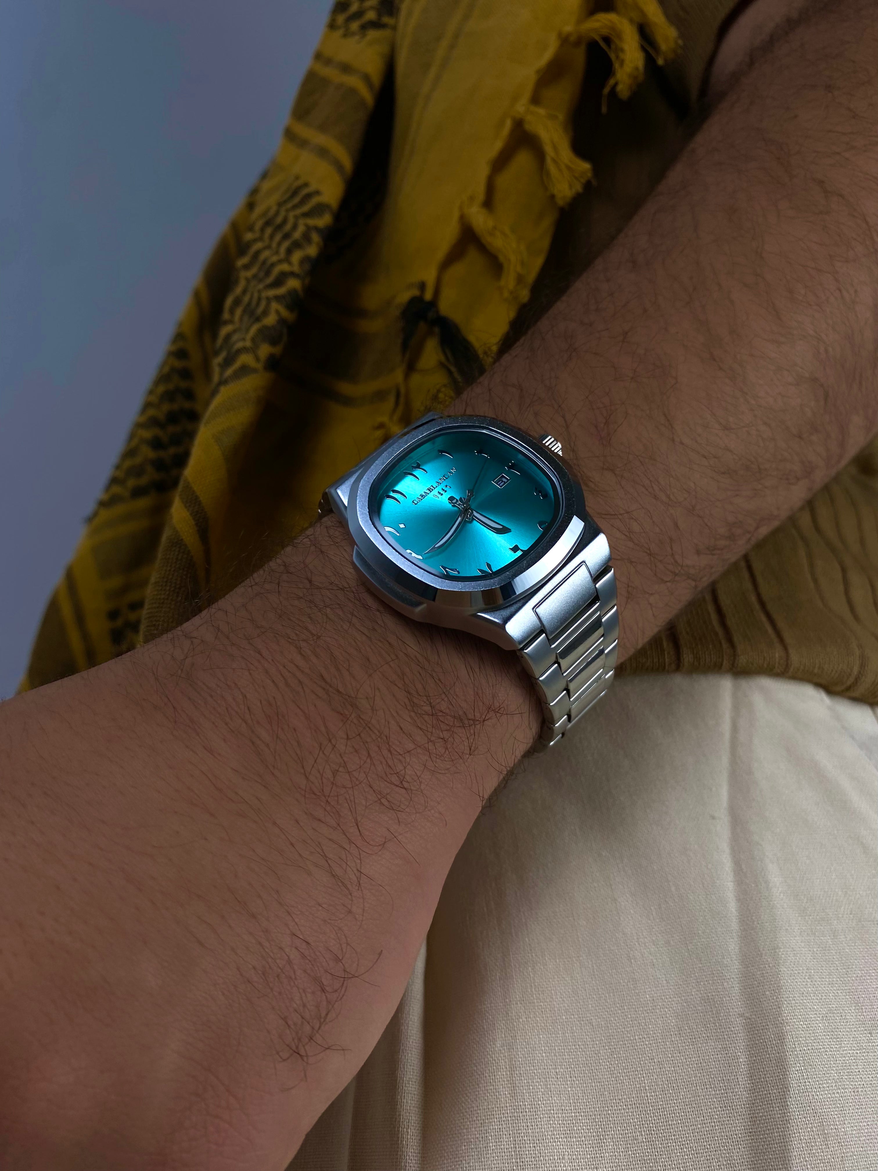 Model wearing a Casablancan Al-Majaz heritage Arabic numerals turquoise dial 43mm Watch with a yellow scarf in the background