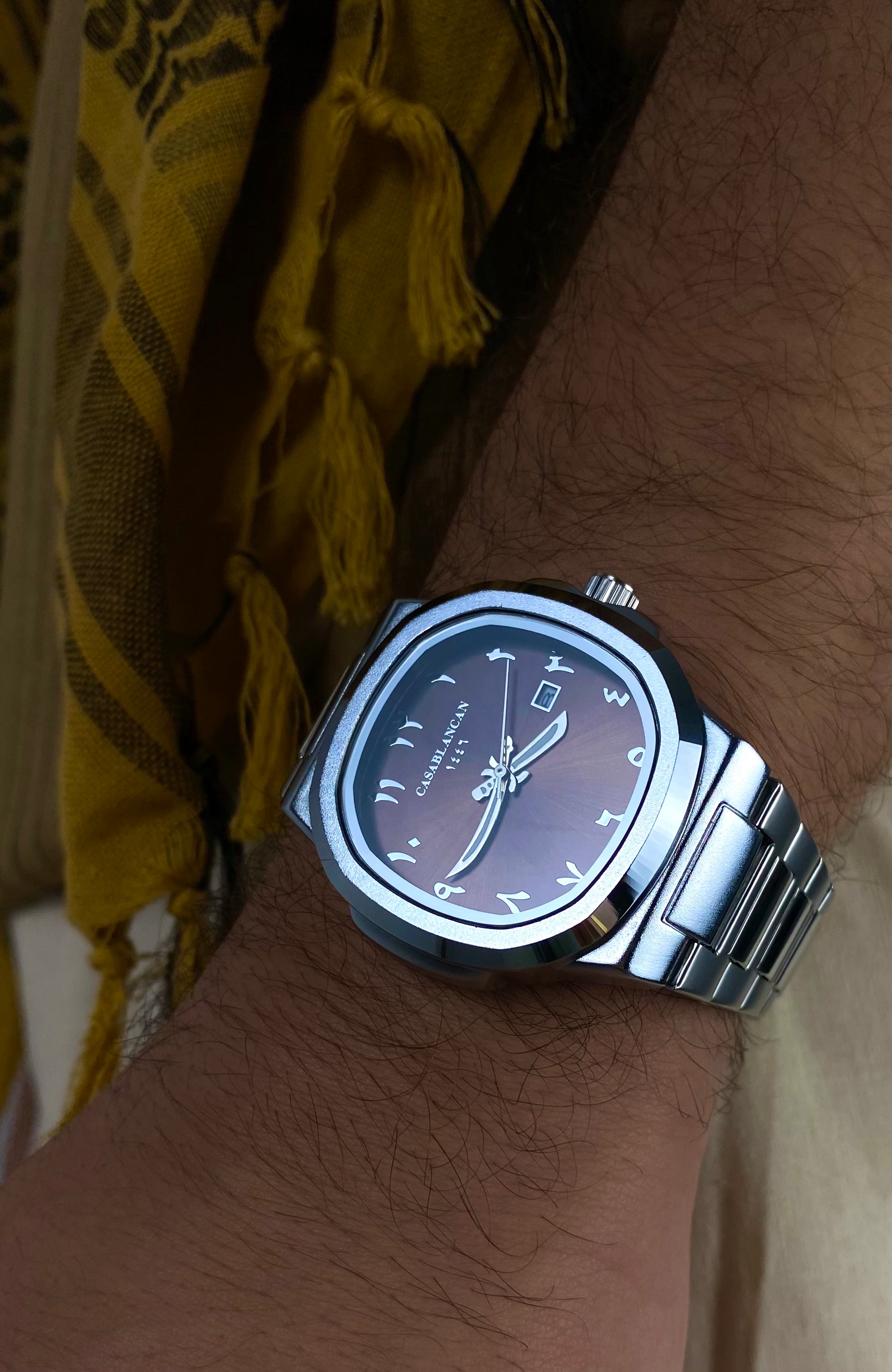 model's Wrist wearing Casablancan Dune Heritage Arabic numerals brown dial 43mm Watch, against a yellow fabric background.