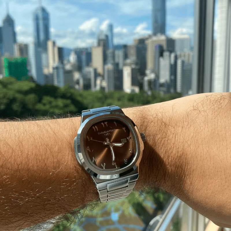 Silver Arabic dial watch on a wrist with a city skyline in the background